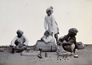 view India: a street conjuror with his musicians, putting a man inside a net and a wicker basket. Photograph, ca. 1900.