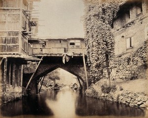 view Kashmir: a built-over bridge on a canal betweeen houses. Photograph by Samuel Bourne.
