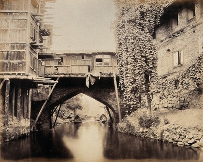 Kashmir: a built-over bridge on a canal betweeen houses. Photograph by Samuel Bourne.