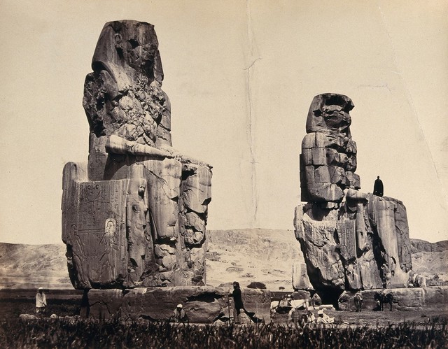 The Statues of the Plain, Thebes, Egypt: a man is standing in the lap of one statue; other men and donkeys at the base. Photograph by Francis Frith, ca. 1858.