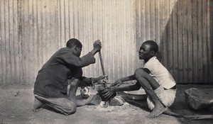 view Umtali, Zimbabwe: two African boys stirring a cooking pot. Photograph by J. Lomas, 1905.