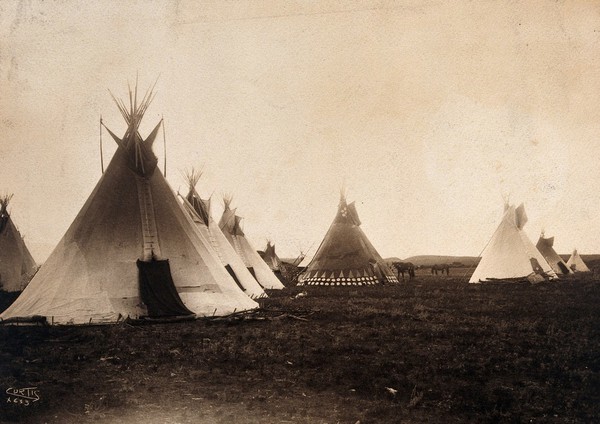 A Piegan encampment, North America: tipis, including a decorated medicine tipi (centre). Photograph by Edward S. Curtis, 1900.