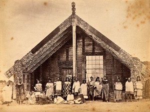 view New Zealand: a group of Maori people in front of a traditional building. Albumen print.