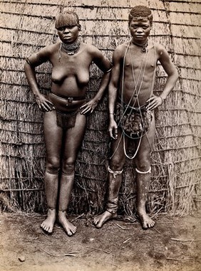 Africa: an African woman and man in front of a kraal hut. Albumen print.