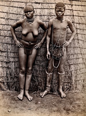 view Africa: an African woman and man in front of a kraal hut. Albumen print.