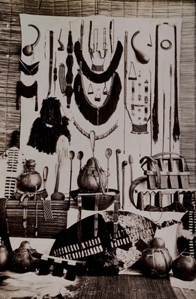 Africa: a display of Zulu shields, mats, pillows, smoking horns, monchies, spoons, baskets, tschinala and amas pots, and beadwork. Albumen print.