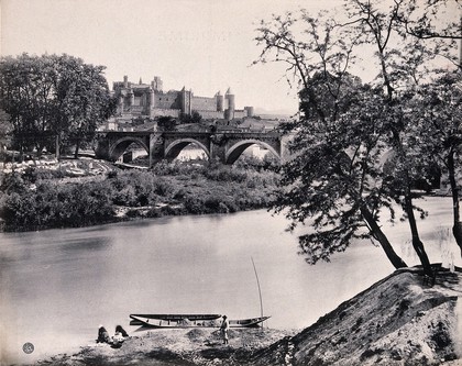 Carcassonne, France: the walled city and bridge over the Aude river; women wash laundry on the river bank and a man shovels grit into a narrow boat. Process print by Bauer, Marchet & C.ie after a photograph.