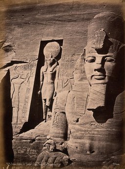 The Abou Simbel temple (the Sun Temple of Ramesses II), Nubia, Egypt: detail of facade showing Ramesses II and the sun god Ra; a man squats in the foreground to show scale. Photograph by Pascal Sébah, ca. 1875.