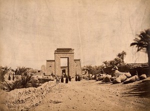 view Karnak Temple, Luxor, Egypt: the Avenue of Rams leading to the propylon of Ptolemy III Eurgetes I; people wearing robes walking on the avenue. Photograph by Pascal Sébah, ca. 1875.