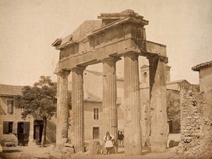 view Athens: the gate of Athena Archegetis in the Roman Agora, Athens; a man in traditional Greek dress poses in the foreground. Photograph by Petros Moraites, ca. 1870.