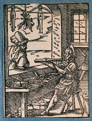 A crossbow maker (bowyer) is working at his workbench, with two finished crossbows and some bolts hanging in the window. Woodcut by J. Amman.