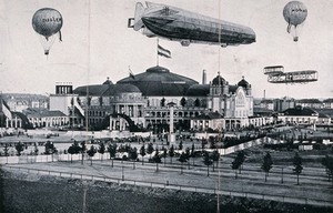 view International Airship Exhibition, Frankfurt, 1909: a Zeppelin airship, an aeroplane and two balloons airborne over the exhibition site. Process print.