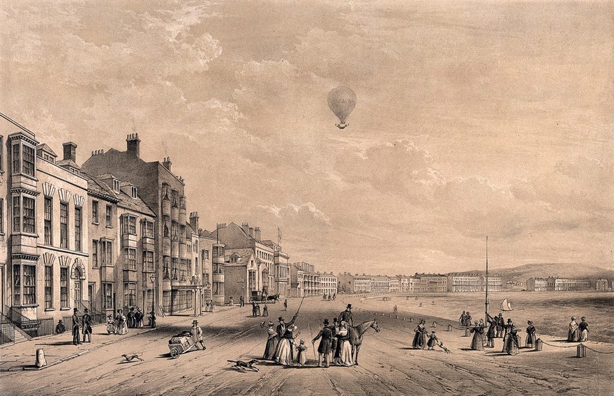 People gathered at the sea front, Weymouth: some are looking up and pointing to a hot-air balloon in the sky. Tinted lithograph.