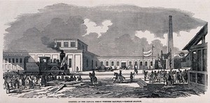 view A train has arrived at a station to be welcomed by crowds of people with banners. Wood engraving.