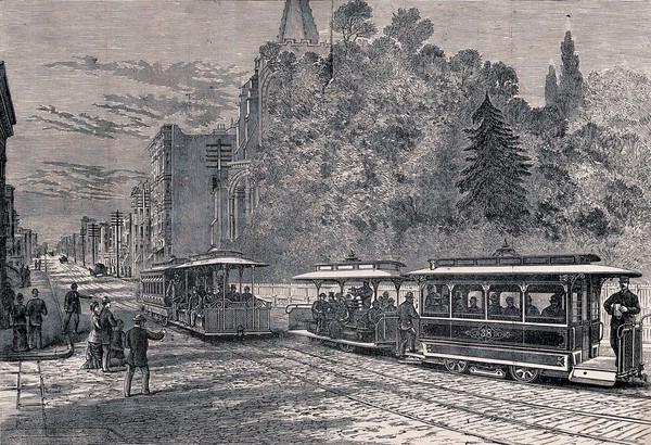 A street scene in San Francisco with people watching as cable-drawn tram cars pass on the road. Process print.