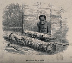 view A man in Africa sitting imprisoned on the ground, with his hands and feet locked into holes made in cut-down tree trunks. Wood engraving after P.B. Du Chaillu, 1867.