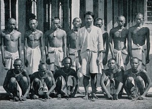 view Thirteen male prisoners in India or Burma ("dacoits", bandits) wearing chains around their necks and ankles. Process print.