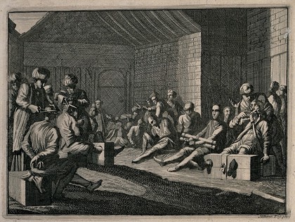 Male prisoners are sitting with their legs in stocks and their hands tied as men in turbans cut off their hair and moustaches. Etching.