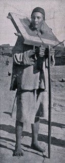 A Chinese man stands carrying the cangue around his neck as a punishment. Process print after a photograph.