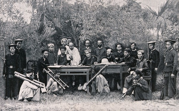 Hanoi, Vietnam: four seated men restrained by the cangue round their necks are being tried for violent crimes by the tribunal of the French resident; armed guards standing by. Wood engraving by H. Thiriat, 1889, after C.E. Hocquard.