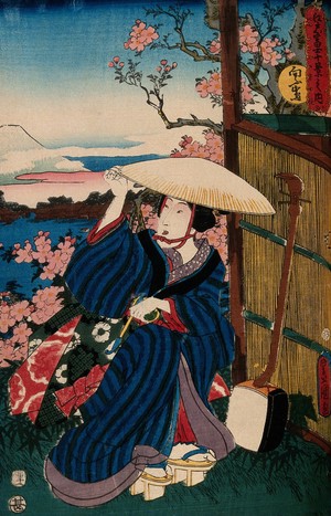 view A kneeling woman in a broad straw hat, holding a pipe; a shamisen rests against the reed fence to the right; the view behind is a view of Fuji from Mukōjima. Colour woodcut by Kunisada, 1854.