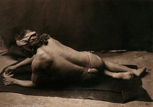 view Zuni medicine man, New Mexico: reclining on a blanket wearing only a loin cloth, showing his back and his face in profile. Photograph by Edward S. Curtis.