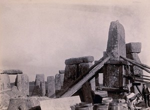 view Stonehenge, England: the straightening of a leaning stone which is attached to a wooden frame and supported by beams and pulleys: raised upright. Photograph, 1901.