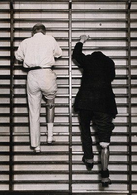 Prostheses: two men with artificial limbs demonstrating their comparative agility by climbing gymnasium bars at St. Thomas' Hospital, London: the man on the left wears a new type of prosthesis. Photograph, ca. 1920.