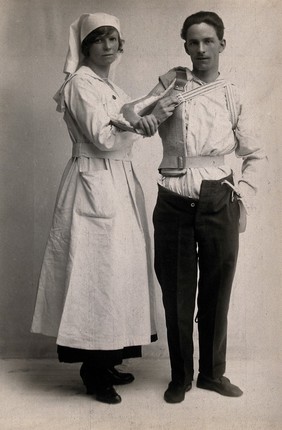 A man wearing an arm support, aided by a nurse. Photograph, 1914/1918.