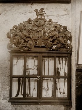 The Barber Surgeons' Guild of Newcastle: surgical instruments in a display case bearing the Guild's coat of arms. Photograph, ca. 1900.