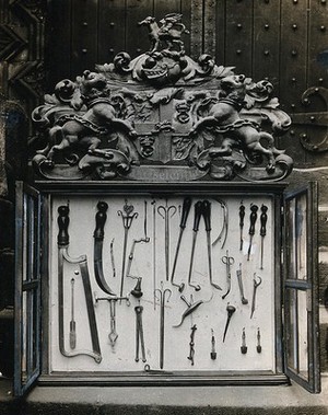 view The Barber Surgeons' Guild of Newcastle: surgical instruments in a display case bearing the Guild's coat of arms. Photograph, ca. 1926.