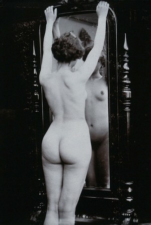 view A young woman, almost full-length, posing naked in a photographic studio, looking at herself in a cheval-glass. Photograph, ca.1900.