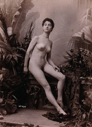 A young woman seated on a low balustrade posing naked.