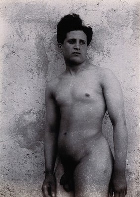 A naked Sicilian male, standing outdoors against a wall. 