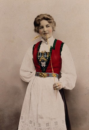 view A young Norwegian woman, posing in a photographic studio wearing peasant dress. Coloured photograph by S. Lund, 1903.