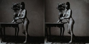 view A young woman posing naked in a photographic studio, standing in front of a table on which is a vase of flowers. Stereo photograph, ca.1900.