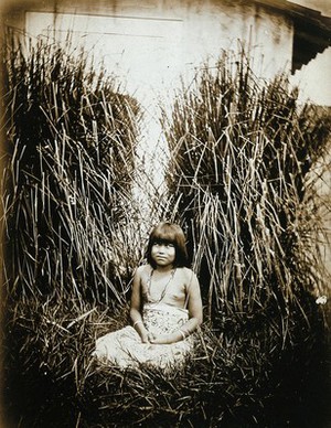 view An Amazonian Indian child, next to a whitewashed wall with tall grasses all around.