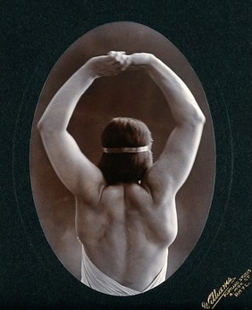 A young woman posing semi-naked, back view, with her arms in the air, in a photographic studio. Photograph by Portland Studio.