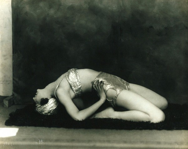 Marguerite Agniel posing leaning back wearing a two-piece costume and matching turban, in a photographic studio.