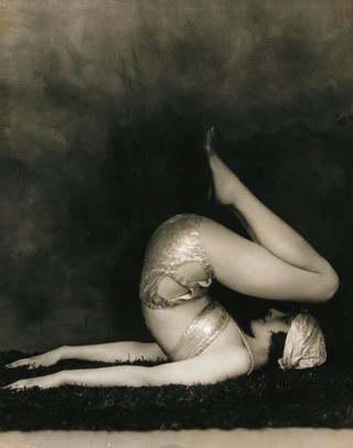 Marguerite Agniel posing with her back arched and feet in the air, wearing a two-piece costume and matching turban.