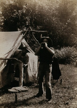 view Two men outside a crude tent, one shouting (?) Photograph, ca.1900.