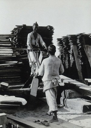 view Two men sawing a baulk of timber in a woodyard, in Korea.