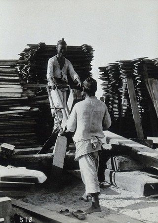 Two men sawing a baulk of timber in a woodyard, in Korea.