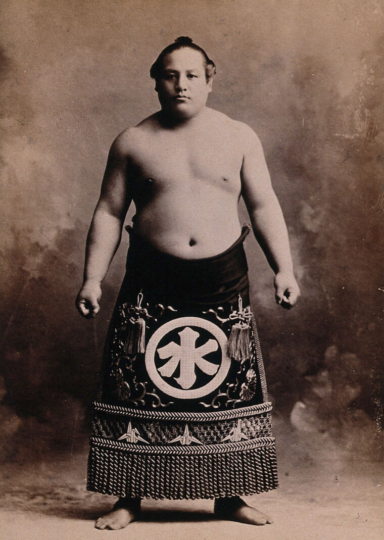 A young sumo wrestler posing in a photographic studio, wearing a richly