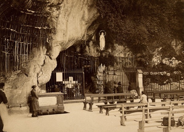 Lourdes, France: the Grotto of Our Lady of Lourdes: pilgrims at the shrine; the sacred water fountain to one side. Photograph, ca. 1870.
