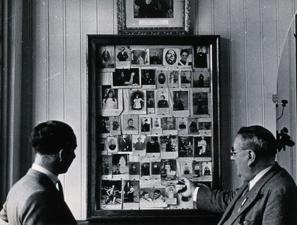 Lourdes, France: framed photographic records of cures examined by Dr. Vallet (right) and a second medical man. Photograph, ca. 1937.