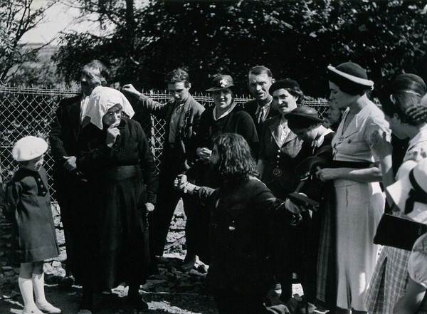 Lourdes, France: a pilgrim kneels with arms outstretched watched by fellow pilgrims ready to perform the Stations of the Cross. Photograph, ca. 1937.