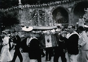 view Lourdes, France: sailors carrying a model of a ship amidst crowds of pilgrims. Photograph, ca. 1937.