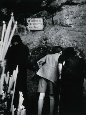 Lourdes, France: the grotto of Our Lady of Lourdes: pilgrims kiss the wall of the cave. Photograph, ca. 1937.