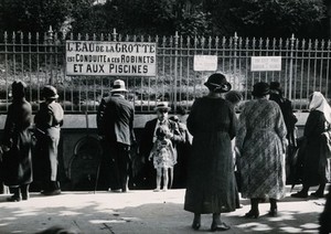 view Lourdes, France: pilgrims at taps bearing sacred water from the Grotto of Our Lady of Lourdes' spring. Photograph, ca. 1937.